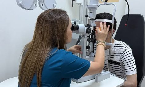 Həkim yarıqlı lampa ilə gənc pasiyentin gözünü müayinə edir